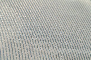 Tırtıklı desenli, muhtemelen kot olan bir kumaşın yakın plan çekimi, yüzeyinde bir desen oluşturan paralel çizgiler içerir. Materyalin üzerindeki yumuşak gölgeler doğal bir şekilde açık hava ortamını işaret eder.