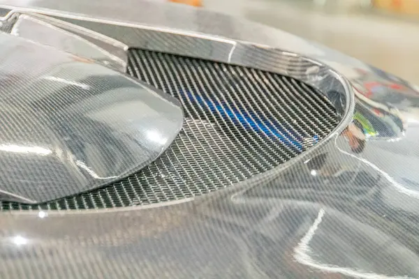 Aerodinamik bileşenler ve motor bölmesi alanına odaklanan bir aracın ön köşesinin yakın plan çekimi büyük, kıvrımlı bir yüzeye sahip bir bileşen görüntüye egemen olur.