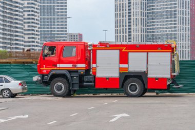 Kırmızı bir itfaiye aracı boş bir otoparkta, merdivenler ve depolama bölmeleri de dahil olmak üzere birkaç itfaiyeci ekipmanı ve bir er Kyiv, Ukrayna 06-06-2024