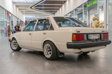 Klasik bir beyaz sedan, muhtemelen sergi ya da sergi alanı içinde, dört kapısı ve açık çatısı olan kapalı bir yerde park halinde. Arka kapak açık, Revali Kyiv, Ukrayna 06-06-2024