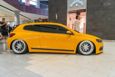 Modifiye edilmiş sarı bir Volkswagen Golf GTI kapalı bir alışveriş merkezinde sergilenmektedir, yan profili belli bir açıyla vurgulanmıştır: Kyiv, Ukrayna 06-2024