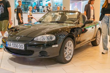 A black Nissan sports car is displayed indoors, positioned at an angle to showcase its front and side profile The vehicle features distinctive headli Kyiv, Ukraine 06-06-2024 clipart