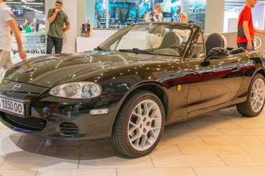 Bir otomobil fuarında kapalı kapılar ardında koyu renkli iki koltuklu spor bir araba sergileniyor. Araç, Ukrayna 06-06-2024 'te ayırt edici far ve stop lambası kullanıyor.