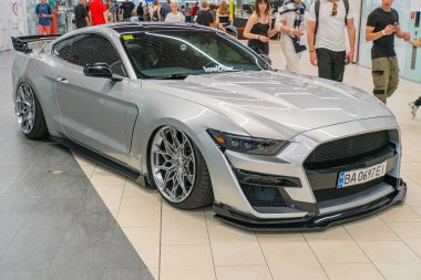 Gümüş renkli bir Ford Mustang spor arabası, aerodinamik ön ve yan profilini gösteren bir açıyla merkezlenmiştir. Araç büyük bir hava girişi olan Kyiv, Ukrayna 06-06-2024