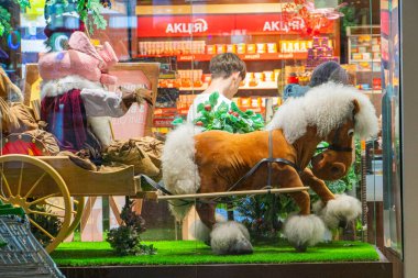 A mannequin dressed as a coachman sits on a toy carriage decorated with miniature trees in front of a glass surface, likely in an indoor setting like Kyiv, Ukraine 06-06-2024 clipart