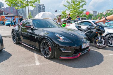 Koyu renkli, şık bir spor araba, diğer arabalar, motosikletler, ağaçlar ve T Kyiv, Ukrayna 06-2024 binalarıyla çevrili bir caddenin yanındaki park alanında park halinde duruyor.