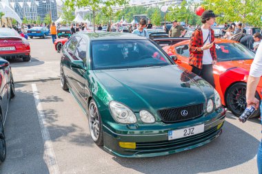 Koyu yeşil bir BMW E30 spor coupe asfalt üzerine park edilmiş beyaz park çizgileri ile çevrili, piyasa değişiklikleri ve çıkartmalarla çevrili bir kişi Kyiv, Ukrayna 06-06-2024 'te duruyor.