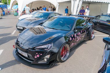 Siyah modifiye bir araba, kırmızı jantlar, pembe aksanlar ve Kyiv, Ukrayna 06-06-2024 sonrası gibi özel modifikasyonlar içeren bir açık hava otomotiv etkinliğinde diğer arabaların arasına park edilmiştir.