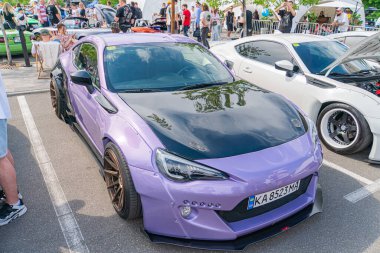 Araba meraklılarının canlı bir sahnesi, parlak, mor bir spor arabanın etrafında toplanıyor, büyük farları olan, beton bir yüzeye park edilmiş araba plakası Pla Kyiv, Ukrayna 06-06-2024