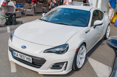 Beyaz bir spor araba asfalt bir zemine park edilmiş, gökyüzü açık, sola dönük, izleyiciye bakıyor. Aracın vitrinleri parlak, aerodinamik Kyiv, Ukrayna 06-06-2024