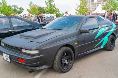 Koyu renk şeması olan özel bir araba, Ukrayna, Kyiv, Ukrayna 06-2024 'ü çağrıştıran kaputun üzerinde canlı grafik tasarımları bulunan bir otomobil fuarında sergileniyor.