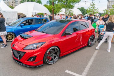 Kırmızı modifiye edilmiş bir spor araba, şık bir tasarım, büyük bir spoiler ve market jantlı açık hava etkinlik alanına park edilmiş durumda. Ukrayna, Kyiv, Ukrayna 06-06-2024 'te birkaç kişi görünüyor.