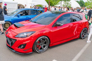 Asfalt bir zemine park edilmiş kırmızı Mazda spor bir araba, koruyucu bir araba kılıfıyla kaplıdır ve bir araba fuarında veya Ukrayna, 06-06-2024 açık hava etkinliğinde insanlarla çevrilidir.