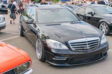 Ön planda, Ukrayna, Kyiv, Ukrayna 06-06-2024 'ün önemli bir bölümünü kaplayan özel jantları ve pazar sonrası modifikasyonlarına sahip siyah bir Mercedes-Benz arabası yer alıyor.