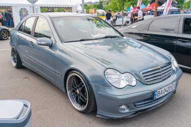 Jantlar ve yan ayna kapakları üzerinde krom aksanlı modifiye edilmiş bir Mercedes-Benz C240 sedan açık havada, şehir merkezinde Kyiv, Ukrayna 06-2024 ile Aftermarket tekerleklerinde duruyor.