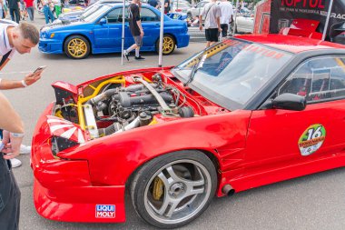 Kırmızı bir spor arabanın kaputu açık, bir araba fuarında veya benzer bir etkinlikte motor ve pazar sonrası parçaları ortaya çıkıyor. Kaportada aerodinamik Kyiv, Ukrayna 06-06-2024 yer alıyor.