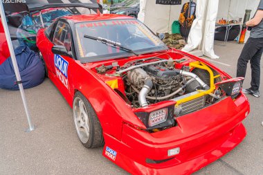 Kırmızı yarış arabasının kaputu açık, motor parçalarını gösteriyor, gövdesinde çıkartmalar ve sponsor logoları var. Araç ön Kyiv, Ukrayna 06-06-2024 'te hasar görmüş.