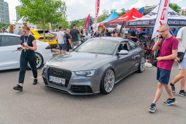 A metallic gray Audi sports car stands center stage in a crowded auto show or car exhibition, with multiple tent-like structures visible in the backgr Kyiv, Ukraine 06-06-2024 clipart