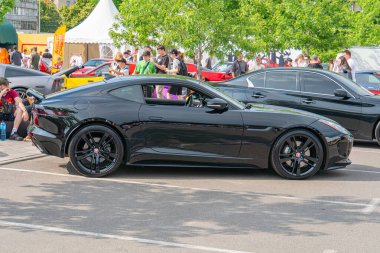 Geniş hava girişli, parlak siyah bir spor araba ve önde gelen bir arka kanat, Ukrayna, Kyiv, 06-06-2024 'teki diğer araçlarla çevrili bir sokak veya park alanına park edilmiş durumda.