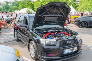 Siyah bir arabanın kaputu asfalt döşemeli bir park yerinde açıkken, diğer bir siyah araba arka kanat spoiler 'ıyla çimlerin üzerine park edilmiş ve ardından Kyiv, Ukrayna 06-06-2024
