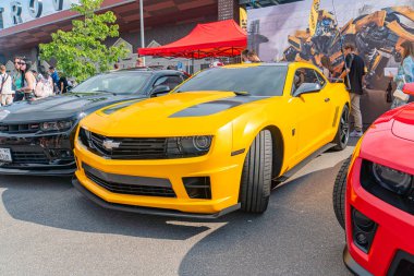 Kaputunda büyük hava girişleri olan parlak sarı bir Chevrolet Camaro Ukrayna, 06-06-2024 'te kırmızı ve beyaz bariyerlerle kaplı bir caddede diğer arabaların yanına park edilmiştir.