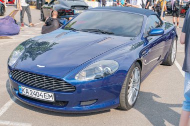 Mavi bir Aston Martin spor arabası bir caddeye park edilmiş, üstü açık bir şekilde kabinin içinde iki koltuk var. Araç çok dilli alaşımlı Whe Kyiv, Ukrayna 06-06-2024