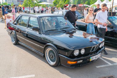 Pazar sonrası tekerlekleri, arka spoiler ve aerodinamik ekipmanı olan siyah bir BMW arabası, Ukrayna, Kyiv, Ukrayna 06-06-2024 'teki kalabalıkla çevrili açık hava etkinliği alanında park halinde bulunuyor.