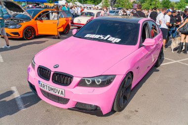 Siyah ve beyaz çizgili pembe bir BMW arabası, Ukrayna, Kyiv, 06-06-2024 otomobiline yayılmış birkaç kişinin yer aldığı canlı bir otomobil fuarı sahnesinin merkezinde duruyor.
