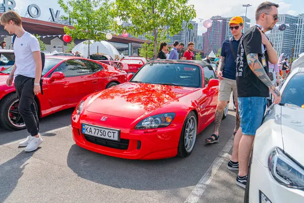 Önünde BENZ yazan muhtemelen bir Mercedes-Benz modeli olan kırmızı bir spor araba, kendisine hayran insanlarla çevrili bir otoparkta oturuyor. Bir grup Kyiv, Ukrayna 06-06-2024