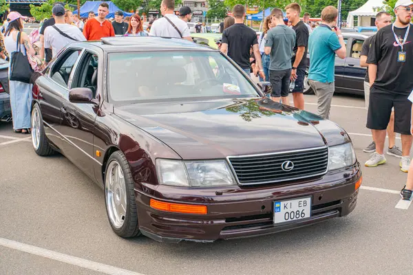 Üzerinde Lexuss amblemi bulunan kahverengi bir sedan sıradan giyinmiş yayalar tarafından çevrelenmiş bir caddede park halinde duruyor. Araç Cu Kyiv, Ukrayna 06-06-2024