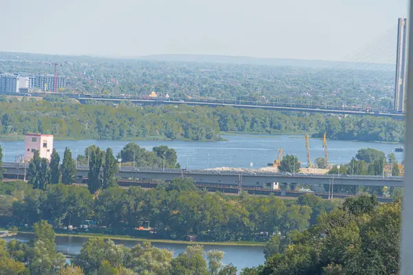 Dinyeper üzerindeki Kiev köprüsü. Nehrin üzerindeki köprüde giden arabalar. Büyük şehrin ve plajın arka planına karşı. Kiev, Ukrayna 10-29-2024.