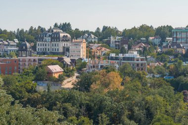 The image is a panoramic view of an urban area with lush green trees and shrubbery in the foreground, surrounding densely packed residential and comme Kyiv, Ukraine 06-06-2024 clipart