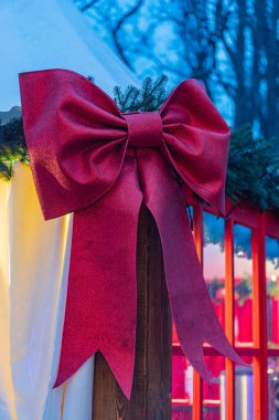 Image showcases a festive red bow with loops and tails, surrounded by pine branches in low light conditions The background is dark, hinting at an outdoor setting The style is realistic and captures clipart