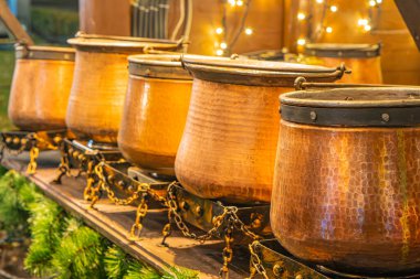 A row of increasing copper kettles with handles and spouts, arranged in an industrial setting with dim lighting, some greenery, warm tone, and a focus on texture and detail clipart