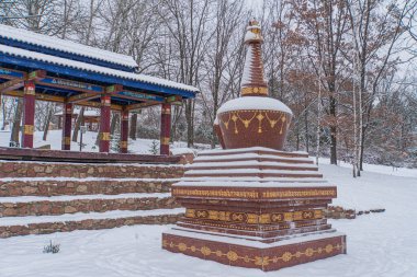 Image of a tranquil winter scene featuring cultural or religious monument with intricate carvings, followed by a pavilion-style building in East Asian architectural style Kyiv, Ukraine 01-14-2024 clipart