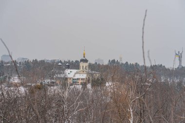 Çıplak ağaçlar, karla kaplı binalar ve bulutlu gökyüzü Kyiv, Ukrayna 01-14-2024