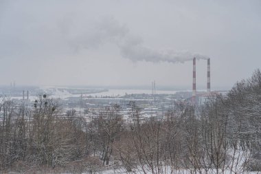 Göl ya da deniz gibi bir su kütlesine uzanan karla kaplı bir kış manzarası ve uzun bacalı sanayi tesisleri Kyiv, Ukrayna 01-14-2024