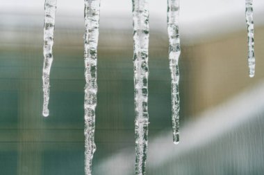 Bir binanın sahanlığındaki sarkıtların yakın plan resmi, şeffaf ve desenli alan derinliği, arkaplandaki başka bir yapının ipucu gri tonlama renk paleti, görünür metin yok