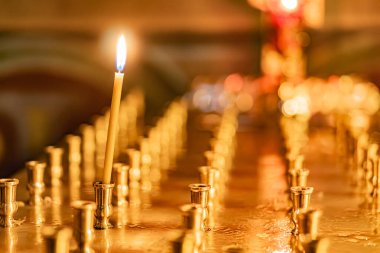 Mimariyi çağrıştıran bulanık bir zemin ile potansiyel kutsal bir alanda gümüş tutacaklı mumların düzenli bir şekilde düzenlendiği huzurlu, ruhani bir sahne.