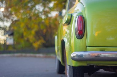 Yirminci yüzyılın ortalarını anımsatan açık mavi alanları olan eski, parlak yeşil bir araba. Yuvarlak kaporta ve krom detaylar içeriyor. İki simetrik arka far ayarı, olası.