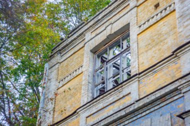 An old, dilapidated brick building with signs of decay and vegetation growth due to prolonged abandonment The window has metal bars and is partially open Natural lighting emphasizes the disrepair clipart