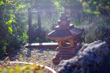 Image of a Japanese garden scene, featuring a traditional lantern chochin on the left The background shows various plants and autumn foliage, with gravel ground Right side has a glimpse of anothe clipart