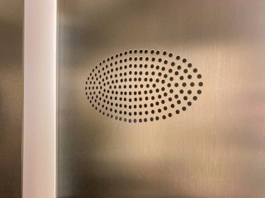 Simetrik, dairesel nokta desenli bir logoyu nötr, yumuşak odaklı bir arka plana yakın plan muhtemelen bir oda ya da asansör gibi bir iç ayar parçası