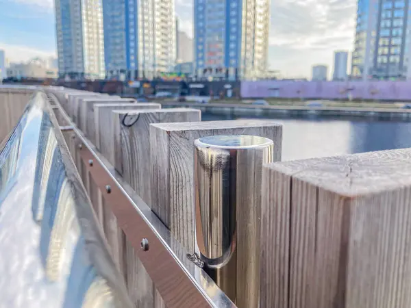 Açık hava sahnesinde ahşap korkulukların üzerinde yansıtıcı, metalik bir cihaz açık gün ışığı altında binalarla çevrili.