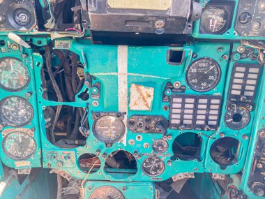 Resim, eski bir askeri uçağın yıpranmış kokpitini tasvir ediyor, çeşitli aletler ve göstergelerle kontrol panelini gösteriyor, mavi-gri, beyaz ve siyah