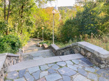 Görüntü, görünmeyen bir istikamete giden taşlı basamaklı sakin bir açık hava sahnesi sergiliyor. Yol bereketli bitki örtüsü ve sonbahar yapraklarıyla çevrili. Bu da sonbaharda yakalandığını gösteriyor.