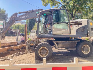 Görüntü, yakınındaki toprak veya moloz yığınları ve arka planda devam eden kaldırım inşaatı ile bir Volvo kompakt yükleyicisini gösteriyor. Açık gökyüzü Kyiv, Ukrayna, 06-15-2024