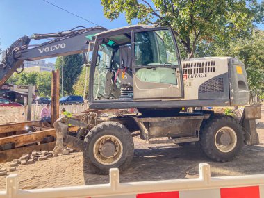 Görüntü, eklemli VOLVO kazıcısının bulunduğu bir inşaat alanında güneşli bir günü resmediyor. Makine hiçbir hareket göstermiyor ve takside operatör Visibili Kyiv, Ukrayna, 06-15-2024 için cam paneller bulunuyor.