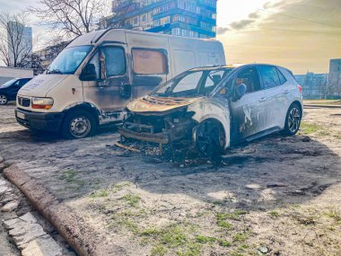 Görüntü iki hasarlı aracı gösteriyor. Bir minibüs ve bir araba açık havada, muhtemelen kentsel alanda. Araçlar yangın veya aşırı ısı hasarı gösteriyor.