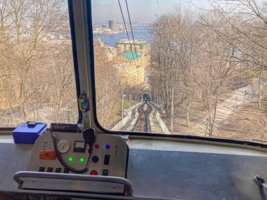 Inside a cable car, looking out at an urban landscape with trees without leaves autumnwinter, reflective water, modern architecture, and overcast sky No people are visib Kyiv, Ukraine, 03-15-2024 clipart